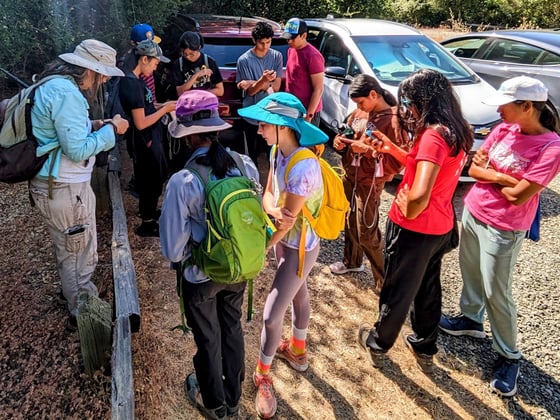 A group of teenagers with stand in a parking lot with GPS devices before setting off to search for geocaches